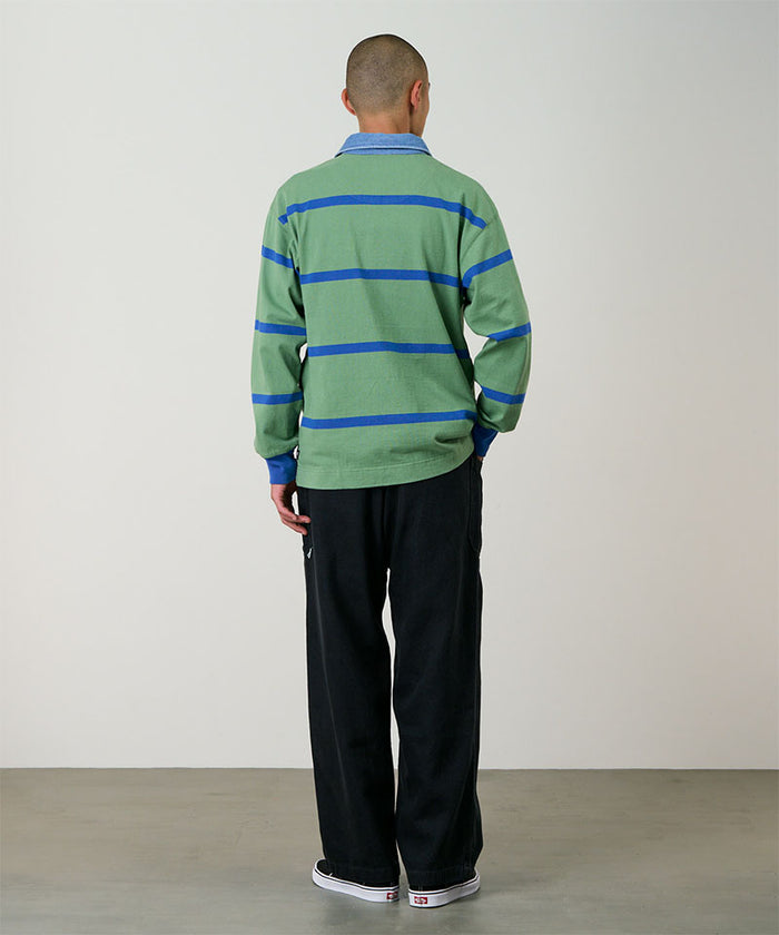 Back view of a model wearing carbon colored Gramicci Hemp Relaxed Pants and a green and blue striped shirt on a light-tone background.