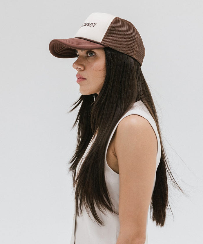 Woman wearing a cream and chocolate brown cap and a white top, facing sideways against a plain background  #color_cream - chocolate brown
