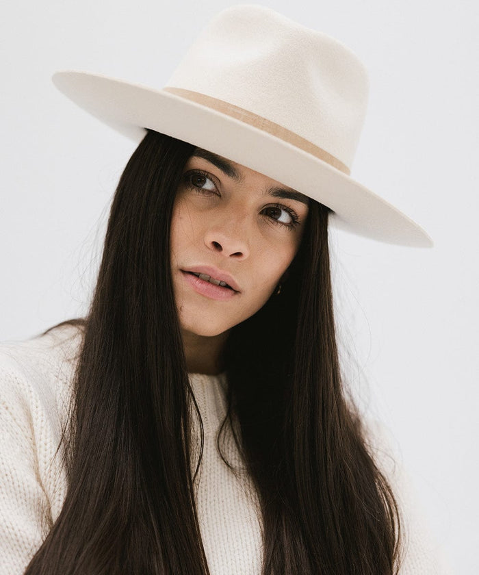 Woman wearing an off white felt fedora hat against a plain background  #color_off white