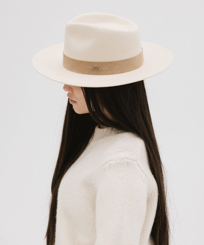 Woman with long hair wearing an off white felt fedora hat with a band and a white sweater, looking sideways against a plain background  #color_off white