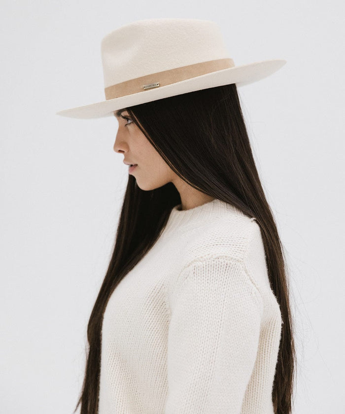 Woman with long hair wearing an off white felt fedora hat with a band and a white sweater, facing sideways against a plain background  #color_off white