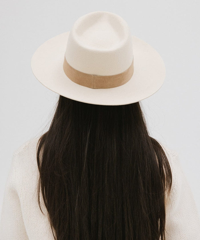 Woman with long hair wearing an off white felt fedora hat with a band facing behind against a plain background  #color_off white