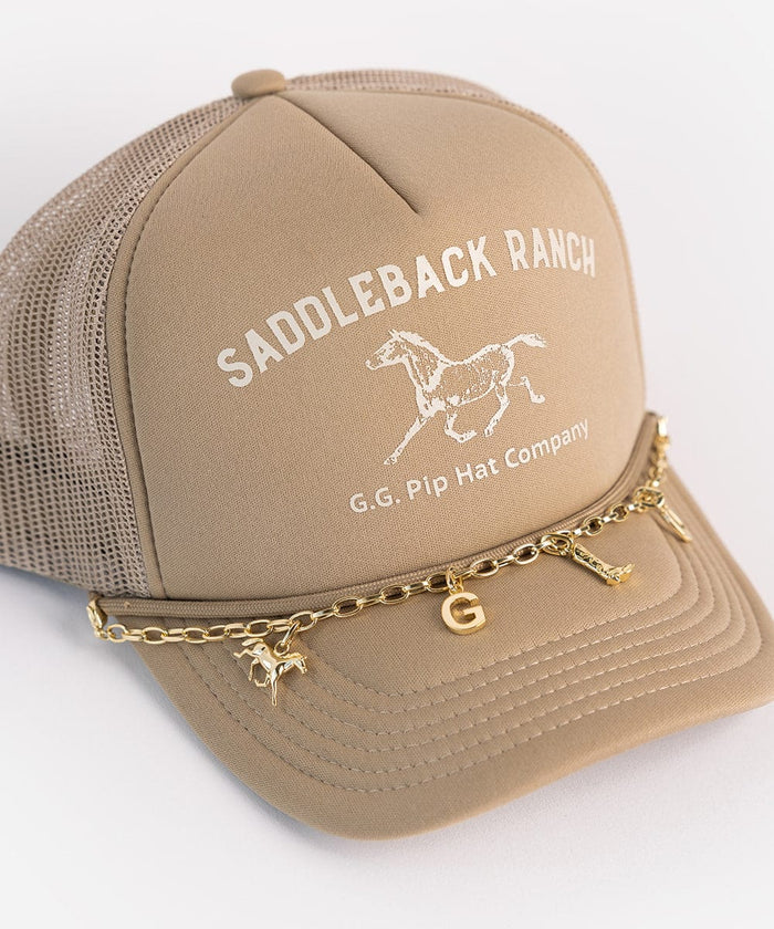 A beige cap with the text 'SADDLEBACK RANCH' and 'G.G. Pip Hat Company' and a horse logo along with a gold chain with letters and a gold horse hat charm on a plain background #color_gold