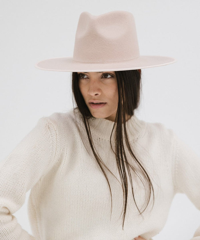 Woman wearing a pale nude colored fedora hat and a white sweater against a plain background #color_pale nude