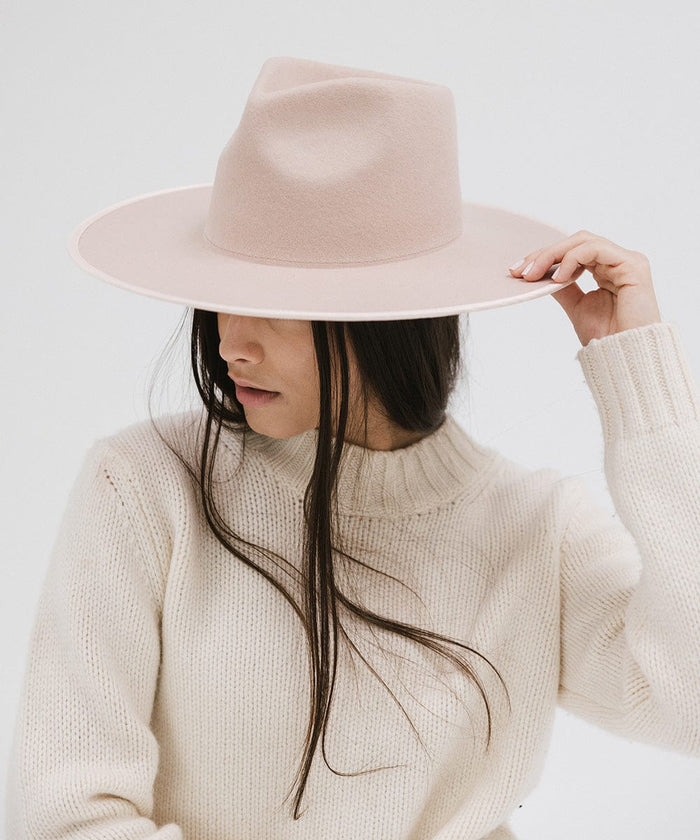 Woman wearing a pale nude colored fedora hat and a white sweater, posing against a plain background #color_pale nude