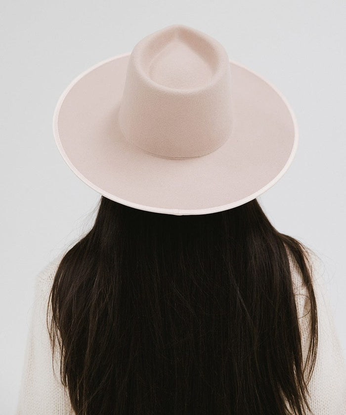 Person with long hair wearing a pale nude colored fedora hat against a plain background #color_pale nude