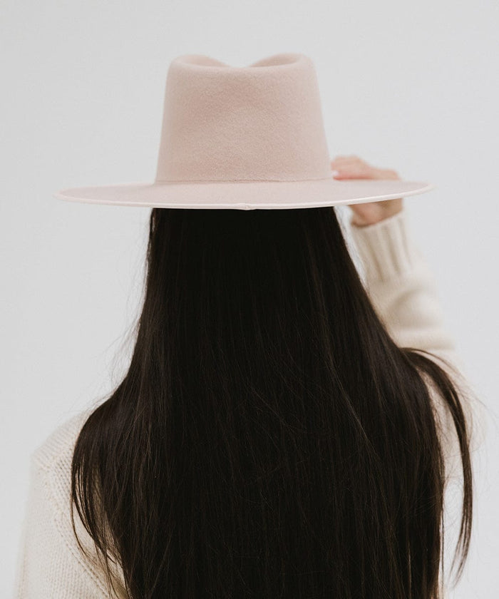 Person with long hair wearing a pale nude colored fedora hat against a plain background #color_pale nude
