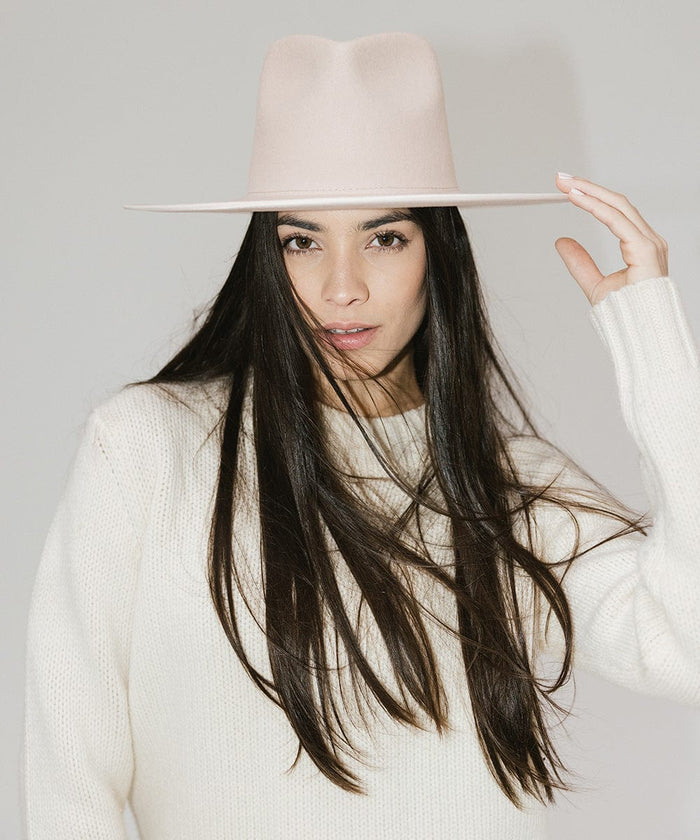 Woman wearing a pale nude colored fedora hat and a white sweater against a plain background #color_pale nude