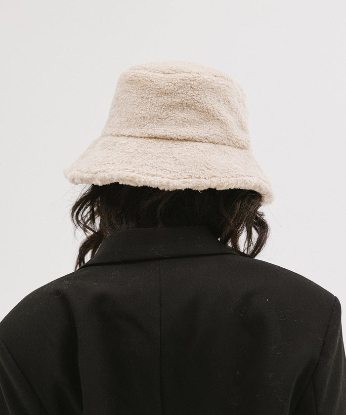 Person wearing a cream sherpa bucket hat and a black coat against a plain background #color_cream