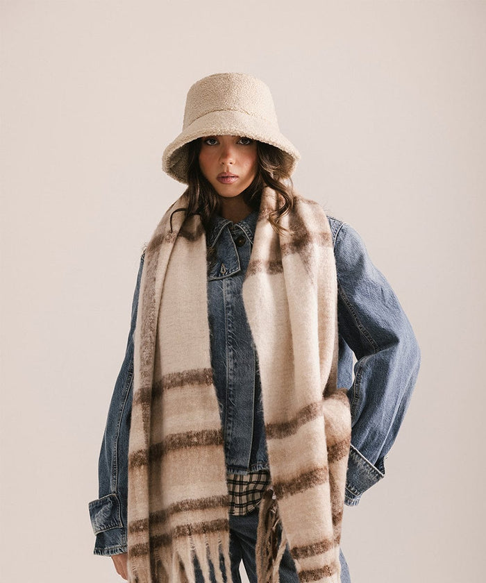 Woman wearing a cream sherpa bucket hat and a black coat against a plain background #color_cream