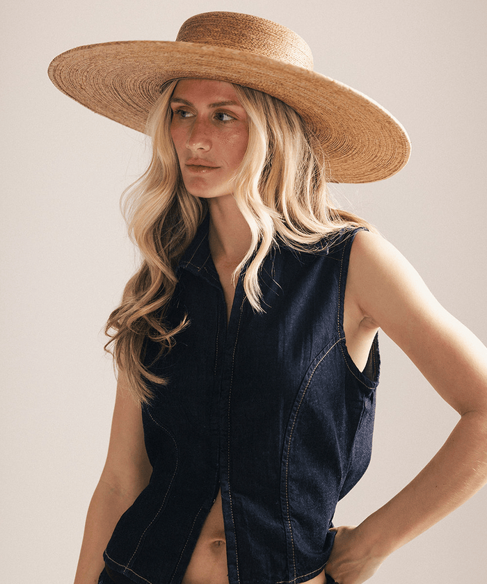 Woman wearing a wide brim boater straw hat against a white background #color_natural brown