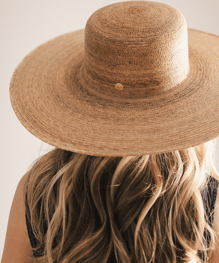 Woman wearing a wide brim boater straw hat against a white background #color_natural brown