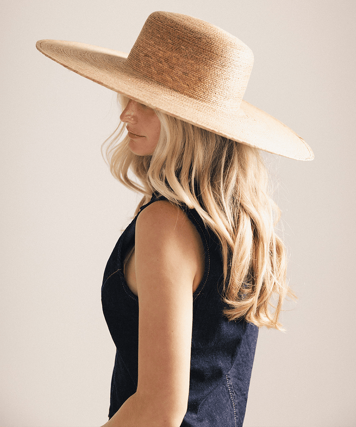 Woman wearing a wide brim boater straw hat against a white background #color_natural brown
