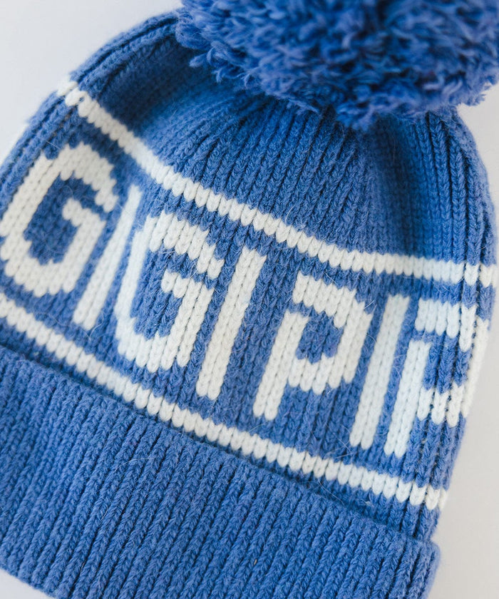 A close up image of an arctic blue colored knit beanie with pom-pom and 'GIGI PIP' branding on a white background #color_arctic blue
