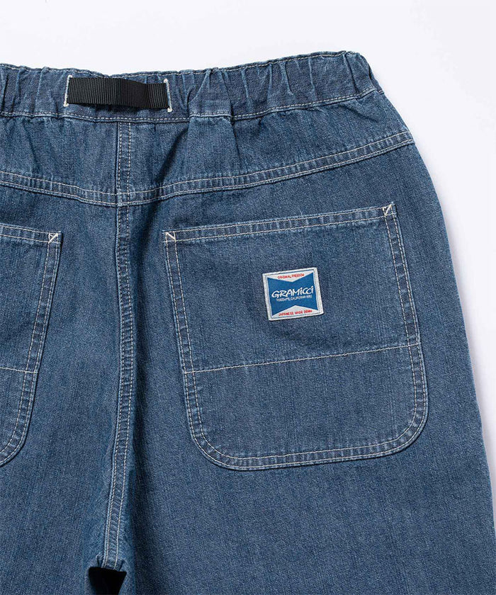 Rear view of a model wearing the Gramicci Japanese Chambray Double Knee pant in blue on a light tone background.