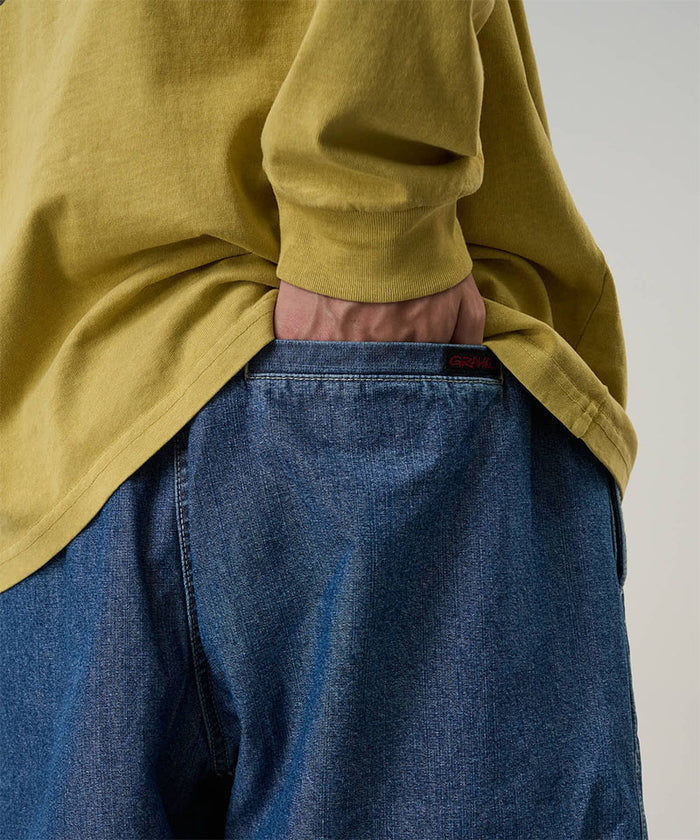 Back view of a model wearing blue Gramicci Japanese Chambray Shorts and a yellow shirt on a light-tone background.