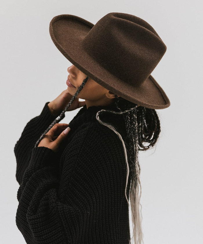 Woman wearing a mix brown colored western hat with a pencil brim and a tall crown, and a black sweater, facing sideways against a plain background  #color_mix brown