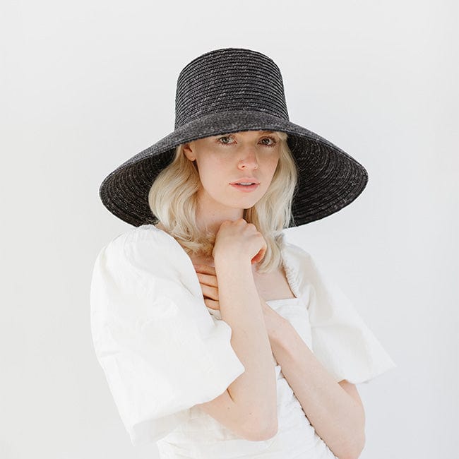 Woman wearing a black boater-style straw hat and a white top against a plain background #color_black