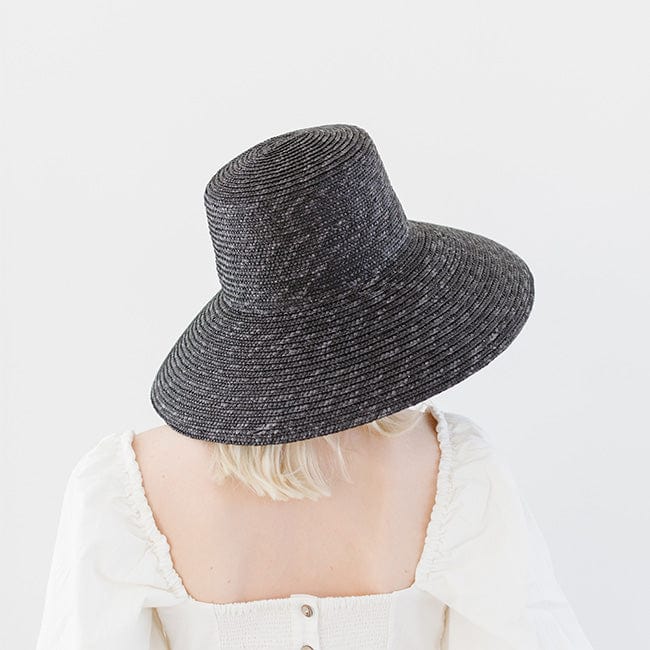 Woman wearing a black boater-style straw hat and a white top, facing behind against a plain background #color_black