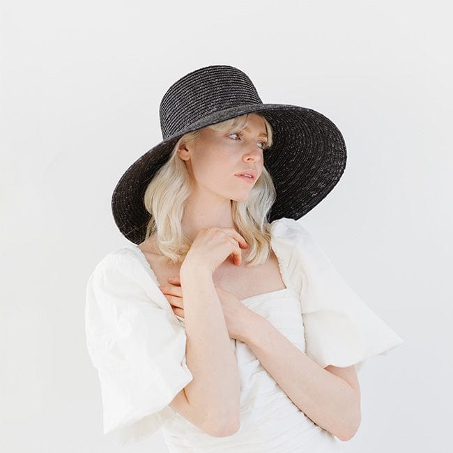 Woman wearing a black straw boater hat and a white top, posing against a plain background #color_black