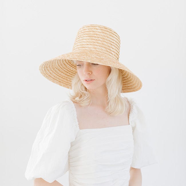 Woman wearing a natural colored straw boater hat and a white top, posing against a plain background  #color_natural