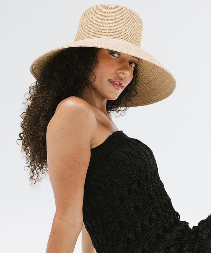 Woman with curly hair wearing a natural colored oversized packable straw bucket hat and a black top against a plain background #color_natural
