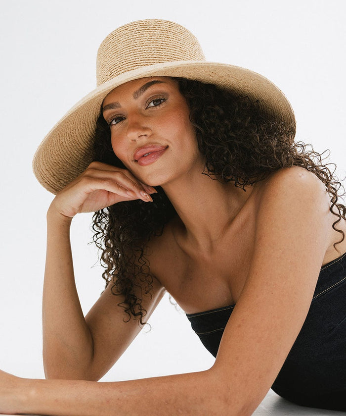 Woman with curly hair wearing a natural colored oversized packable straw bucket hat against a plain background #color_natural