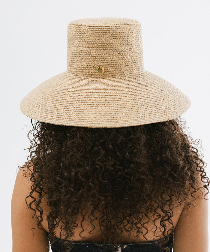 Person with curly hair wearing a natural colored oversized packable straw bucket hat facing behind against a plain background #color_natural