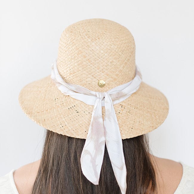 Woman wearing a natural colored packable straw hat with a band facing behind against a plain background #color_natural