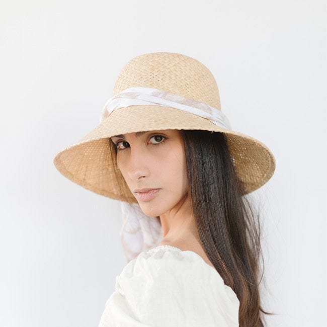 Woman wearing a natural colored packable straw hat with a band and a white top, posing against a plain background #color_natural