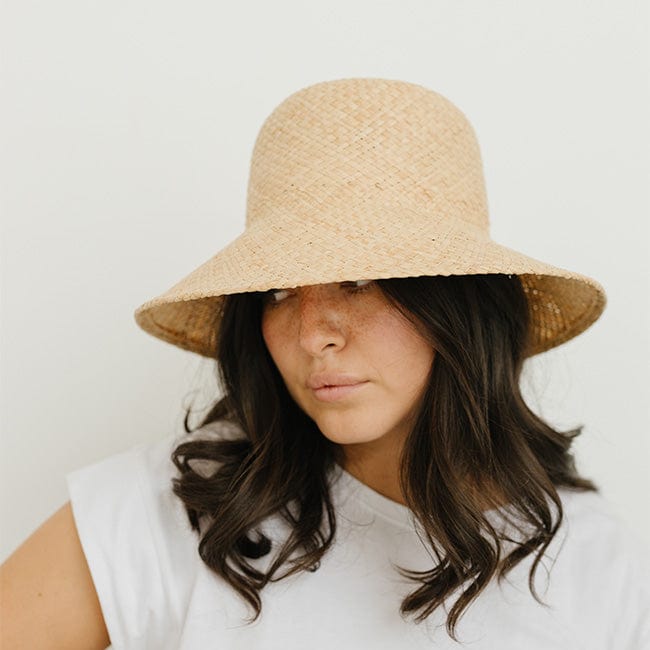 Woman wearing a natural colored packable straw hat and a white t-shirt, looking sideways against a plain background #color_natural