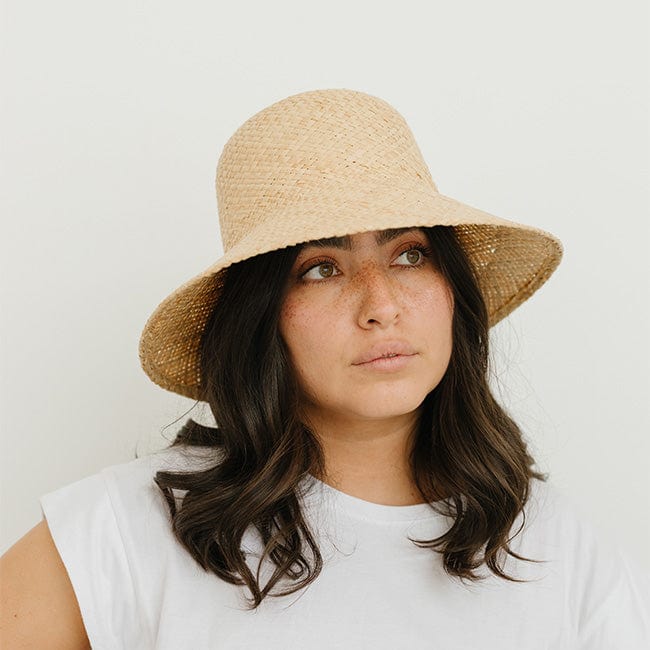 Woman wearing a natural colored packable straw hat and a white t-shirt against a plain background #color_natural