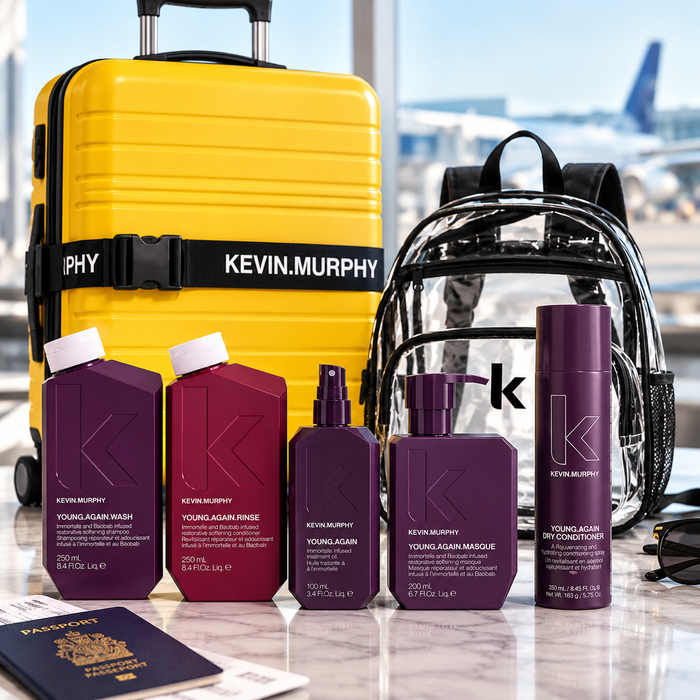 Kevin Murphy Young Again Dry Conditioner and wash set displayed with a yellow suitcase, clear backpack, passport, and sunglasses on a marble surface with an airport window background.