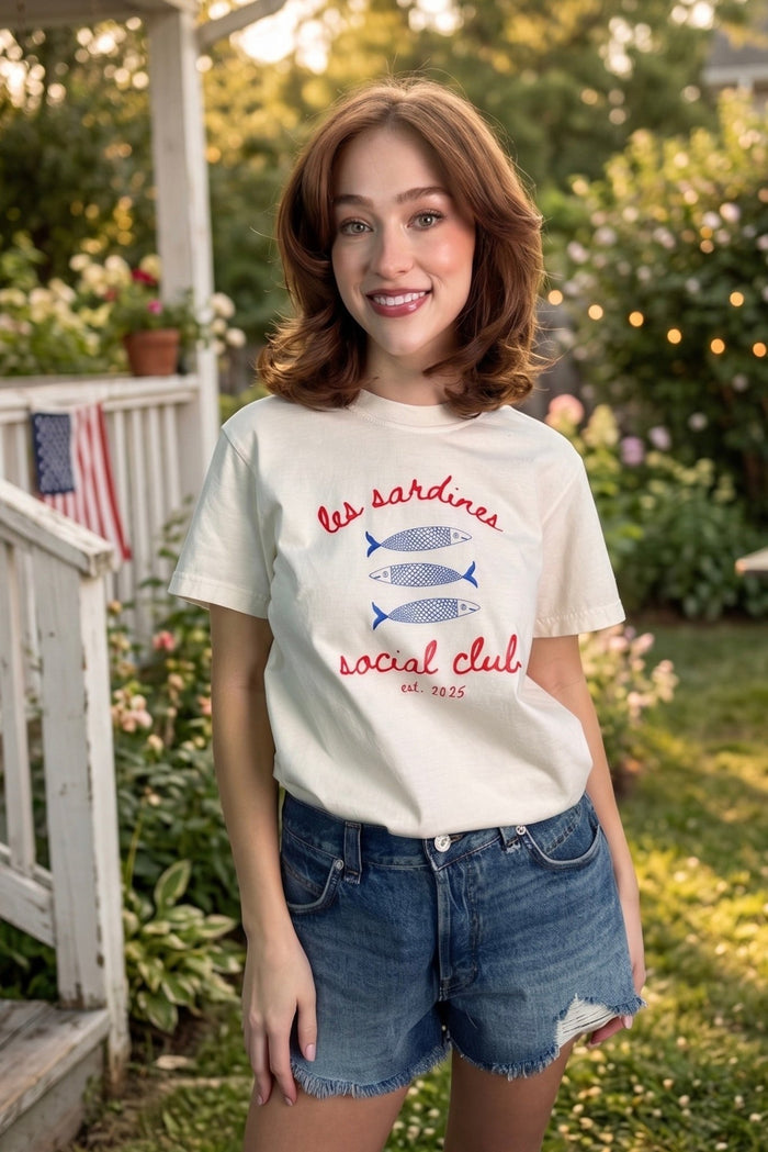Americana graphic tee with red and blue sardine club print styled with denim shorts for Fourth of July outfits, summer country concerts, patriotic boutique fashion, lake days, BBQ parties, and casual Americana looks from Sand + Charcoal Boutique.