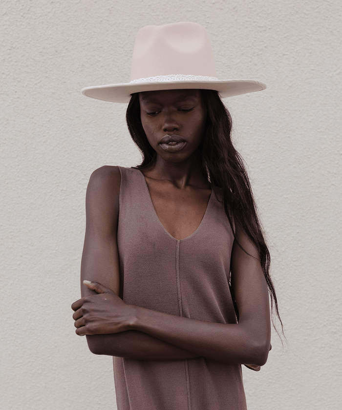 Woman wearing a cream hat with a white lace band and a brown top against a plain background #color_white