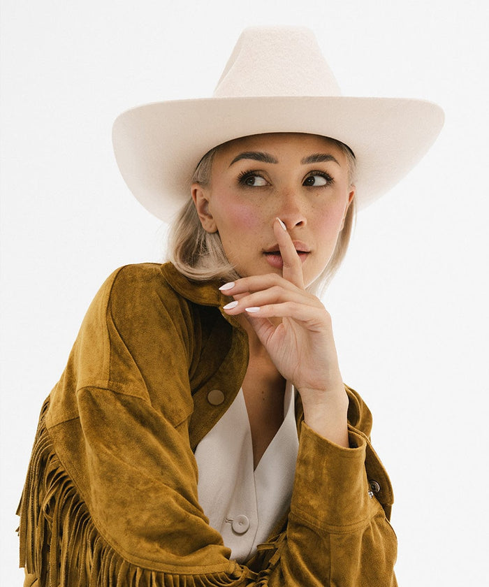 Woman wearing a cream cowboy hat and a mustard colored jacket against a plain background #color_cream