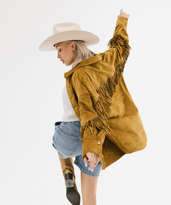 Woman wearing a cream cowboy hat, a mustard colored jacket and denim shorts, posing against a plain background #color_cream