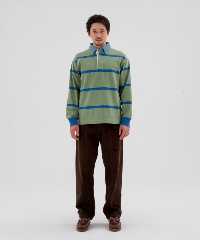 Model wearing a olive and blue striped Gramicci Langdon Rugby Shirt and brown pants on a light-tone background.