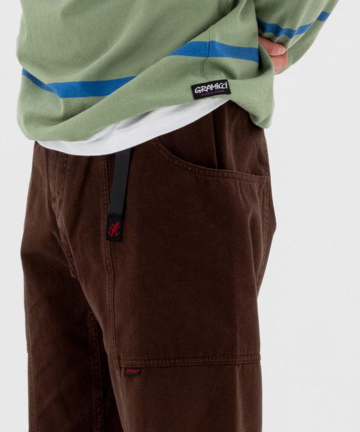 Model wearing brown Gramicci Pants and a green and blue stripped shirt on a light-tone background.