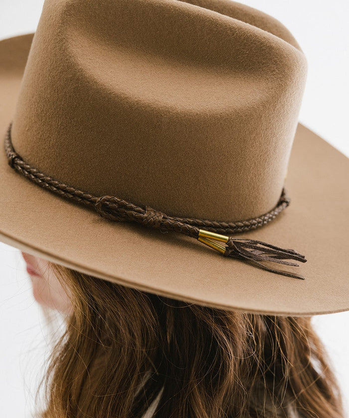 A tan cowboy hat with a brown lasso braided hat band, worn by someone against a plain background  #color_brown
