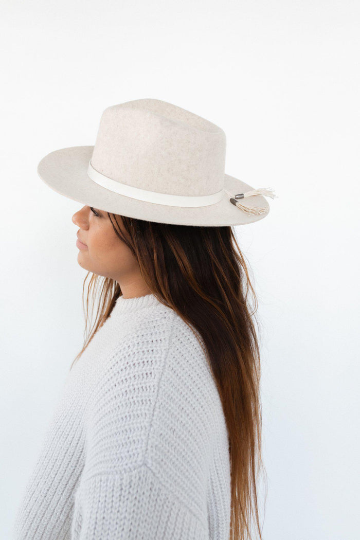 Woman wearing an ivory colored hat with an off white leather band with tassels and a white sweater, facing sideways against a plain background #color_off white