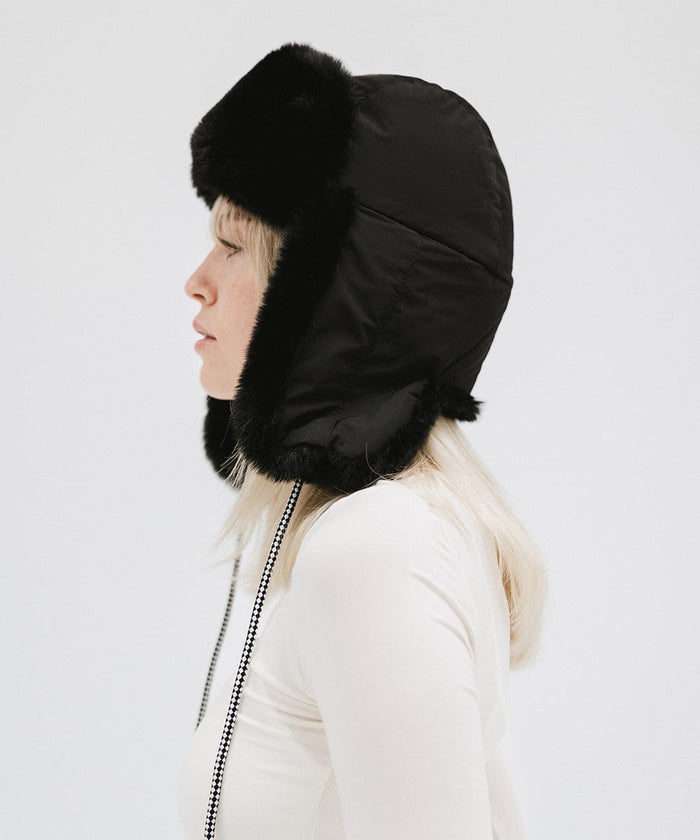 Woman wearing a black fur-trimmed hat and a white top, facing sideways against a plain background #color_black