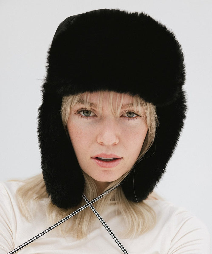 Woman wearing a black fur-trimmed hat against a plain background #color_black