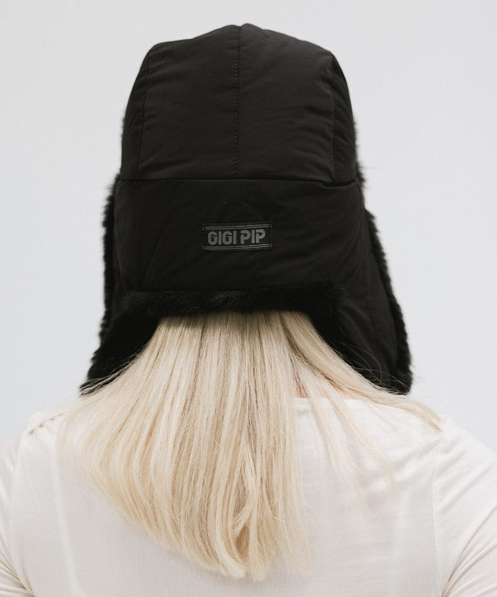 Person wearing a black fur-trimmed hat and a white top against a plain background #color_black
