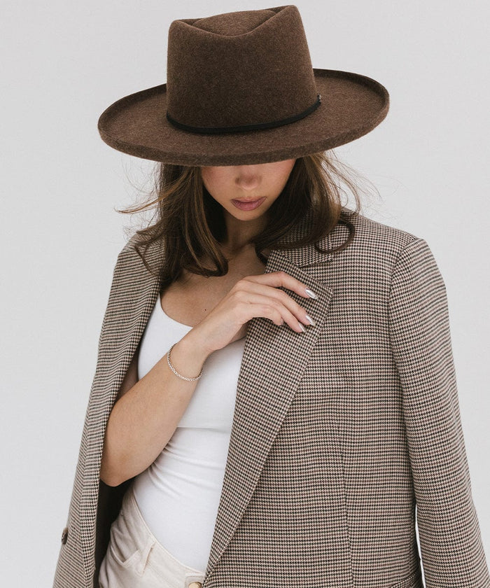 Woman wearing a mix brown Lennon pencil brim fedora hat with a hat band and a white top with a coat, posing  against a plain background #color_mix brown