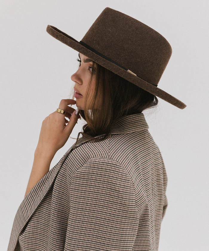 Woman wearing a mix brown Lennon pencil brim fedora hat with a hat band and a coat, posing sideways against a plain background #color_mix brown
