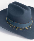 A blue cowboy hat with a hat band and a gold chain with letter hat charms making up the word 'COWGIRL' on a plain background #color_gold