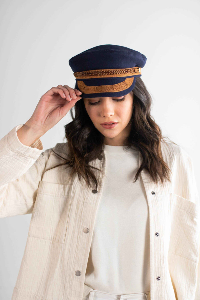 Woman wearing a navy and gold colored lieutenant cap and a white t-shirt inside a cream shirt, posing against a plain background #color_navy