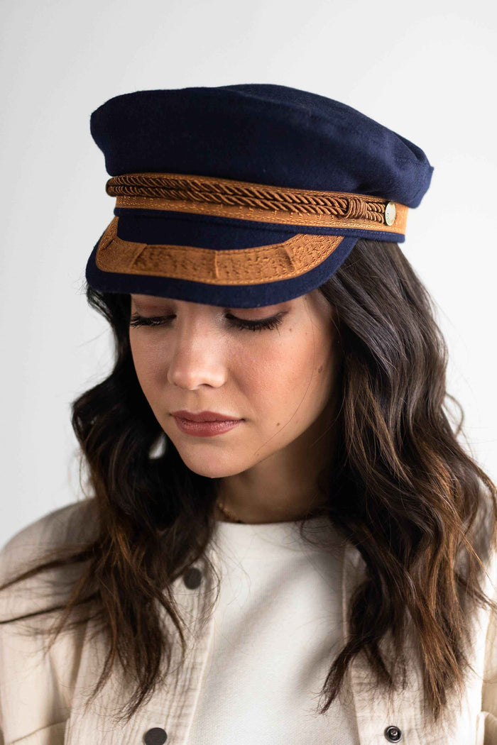 Close up image of a woman wearing a navy and gold colored lieutenant cap and a white t-shirt inside a cream shirt against a plain background #color_navy