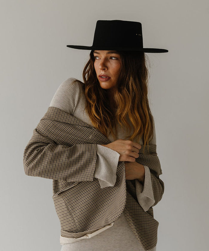 Woman wearing a black boater hat and a white top with a coat, facing sideways against a plain background #color_black